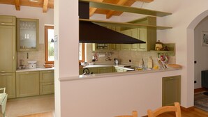 A kitchen with wooden beams, green cabinets, and a large window.