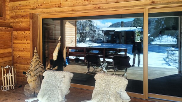 A wooden cabin interior with a large sliding glass door leading to a snowy outdoor area.