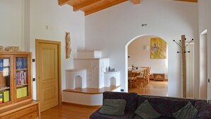A living room with a wooden ceiling, a sofa, a bookshelf, and a dining area in the background.