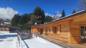 A wooden cabin with a snow-covered ground, a wooden deck, and a clear blue sky.