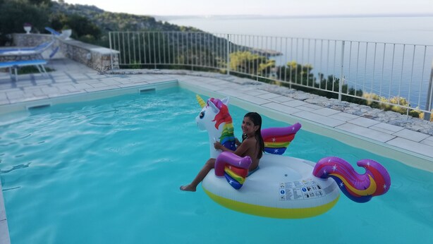 Ett barn sitter på en uppblåsbar enhörning i en pool med utsikt över havet.