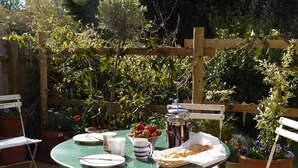 Un área de comedor al aire libre con una mesa dispuesta para dos personas, rodeada de macetas con plantas y una valla de madera.