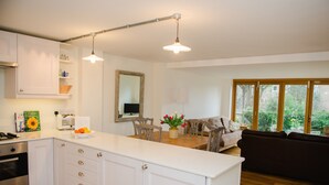 Una cocina moderna con armarios blancos, una isla central y un comedor con mesa y sillas de madera.