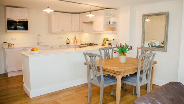 Una cocina moderna con armarios blancos, una mesa de comedor de madera y sillas tapizadas en gris.