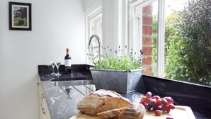 Uma cozinha com bancada de mármore, uma barra de pão, uvas e um vaso de planta.