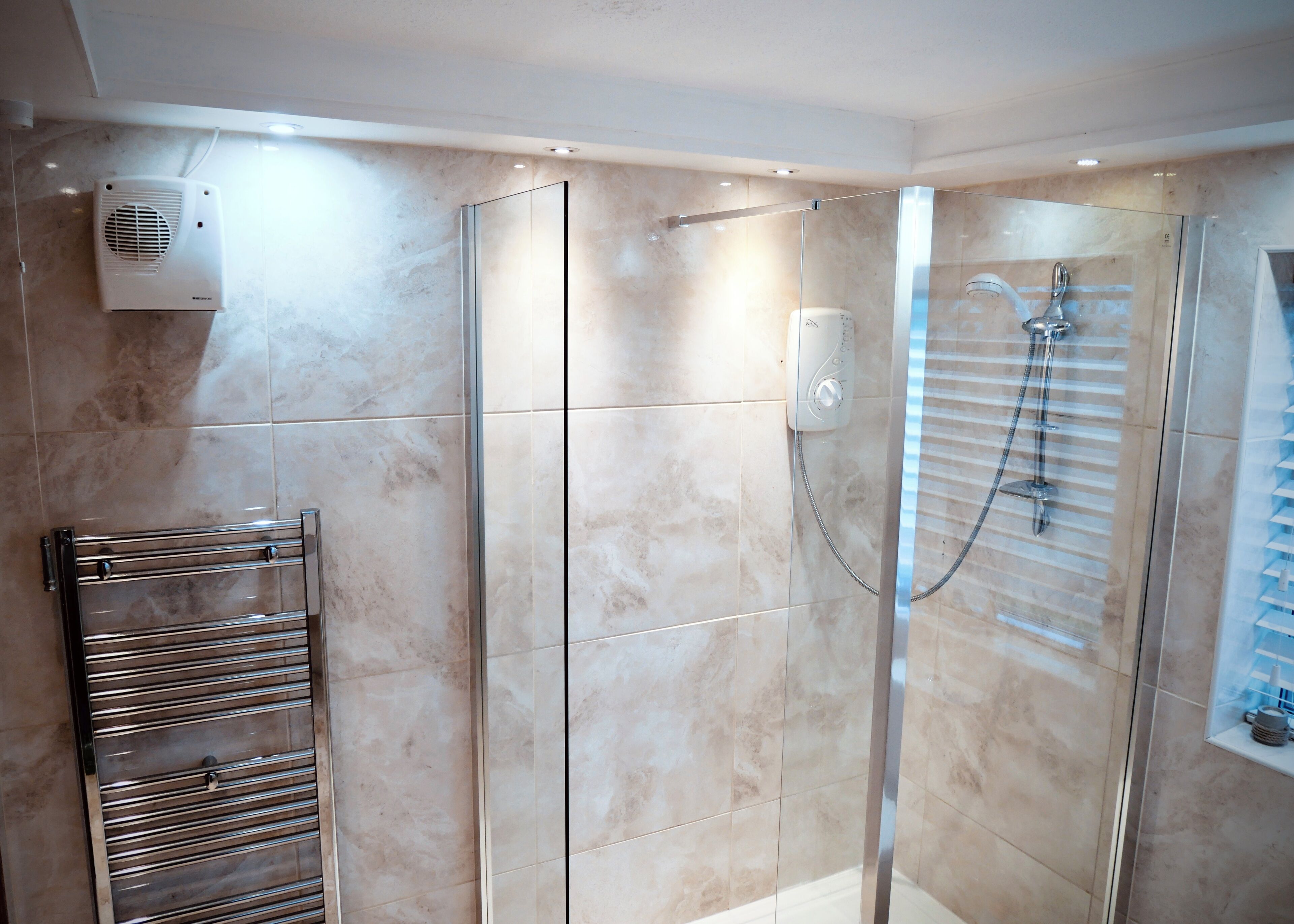 A modern bathroom with a glass shower enclosure, a built-in heater, and a towel rack.
