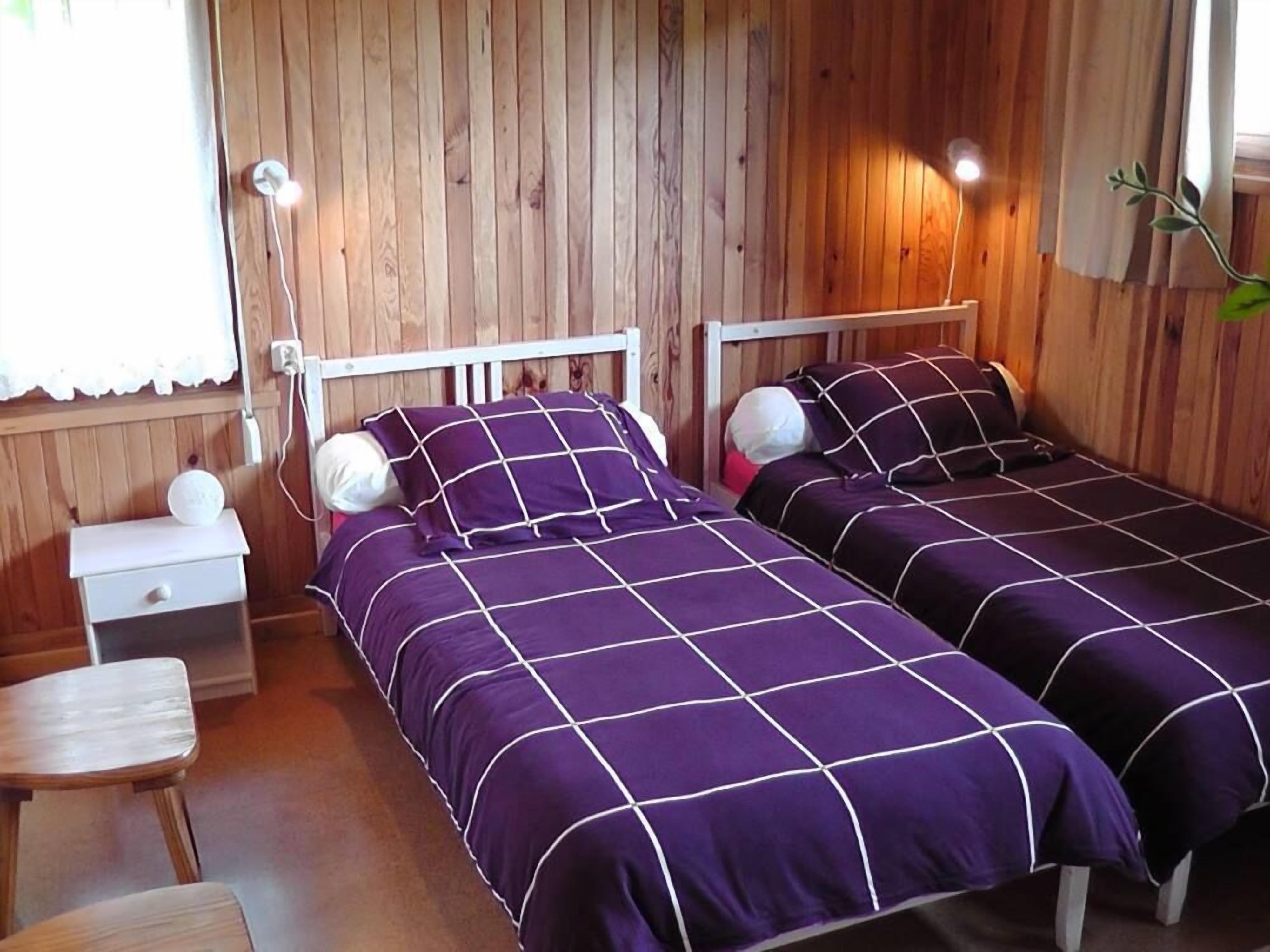 Ein Zimmer mit zwei Betten, Holzwänden, einem Nachttisch, einer Lampe und einem kleinen Tisch.