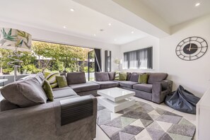 A modern living room with a sectional sofa, a coffee table, and a large window offering a view of greenery.