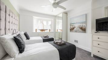 A bedroom with two beds, a ceiling fan, a large window with a view, a painting, and a TV on a dresser.
