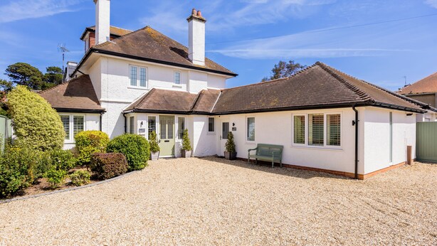 A two-story house with a gravel driveway, a green bench, and a white exterior.