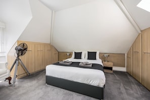 Ein modernes Schlafzimmer mit einem großen Bett, einem Holzschrank und einem Standventilator.