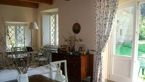 Une pièce chaleureuse avec une table en bois, des chaises blanches, un petit meuble blanc et une fenêtre donnant sur le jardin.