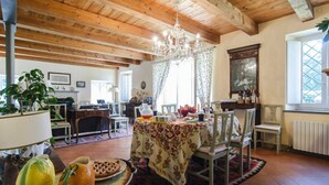 Une salle à manger spacieuse avec un plafond en bois et un lustre, une table dressée pour le repas, et une vue sur l’extérieur par une fenêtre.