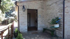 Une façade en briques, une rambarde en bois, une porte, un banc et des plantes en pot.