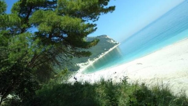 Une plage avec une eau d’un bleu limpide, un rivage sablonneux et un promontoire rocheux.