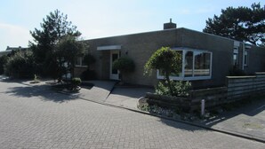 Un bâtiment moderne à deux étages, doté d’une façade en briques, d’un toit plat et d’un petit jardin à l’avant, où l’on trouve une variété de plantes.