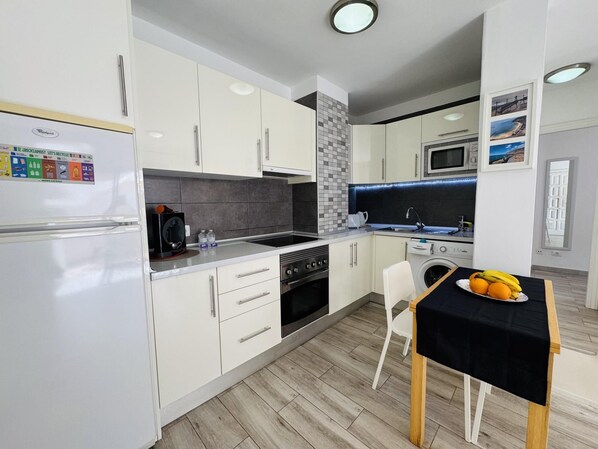 Une cuisine moderne avec des armoires blanches, un four encastré, un four à micro-ondes et un lave-vaisselle. On y trouve également un coin repas avec une table et des chaises, ainsi qu’un réfrigérateur orné du logo Whirlpool.
