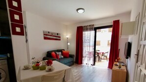 A living room with a sofa, a dining table with chairs, a TV, and a sliding glass door leading to an outdoor area. - Moon Holiday Home in Los Cristianos (Los Cristianos)