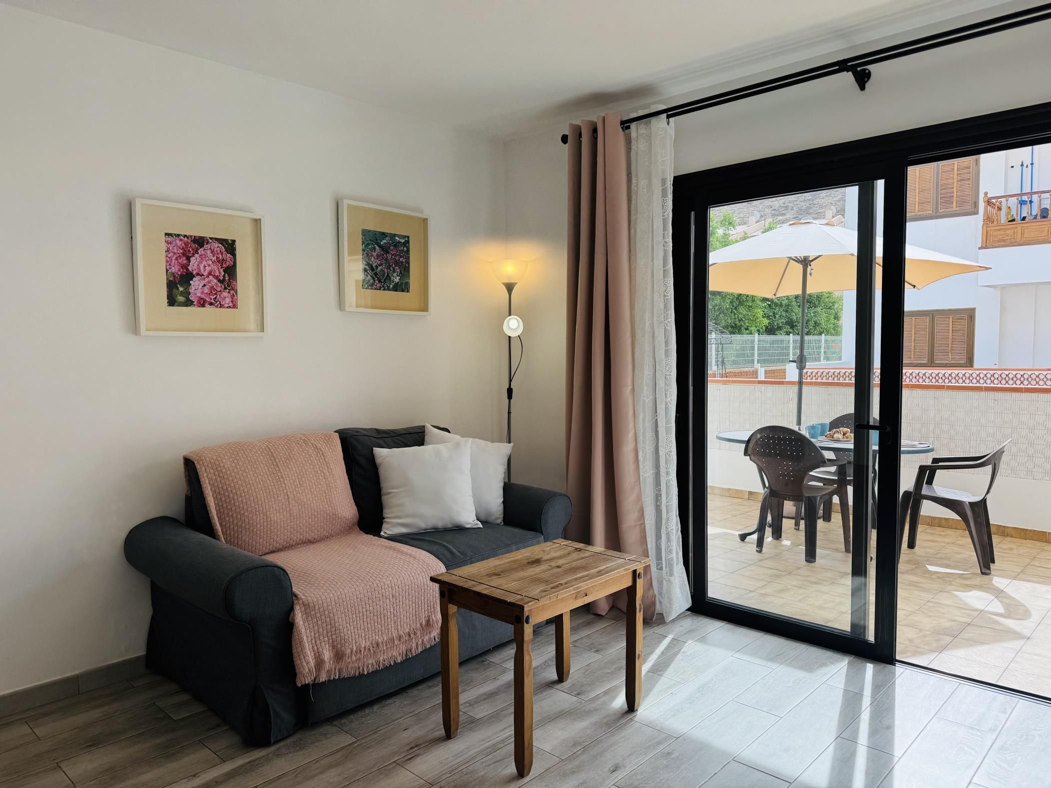 En stue med sofa, sofabord og en skydedør til en udendørs terrasse med bord og stole.
