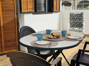 A round table with a white tablecloth, surrounded by black chairs. There are blue cups, a plate with food, and a glass of wine on the table.