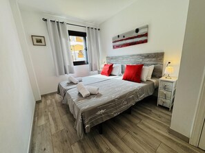 A double bed with a grey and white patterned bedspread, two red pillows, and a white headboard.
