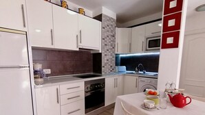 A modern kitchen with white cabinets, a built-in oven, and a microwave. There is a dining area with a table set for two. - Moon Holiday Home in Los Cristianos (Los Cristianos)