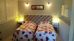 Quarto com duas camas, cada uma com colcha florida, luminárias de cabeceira e um quadro na parede.