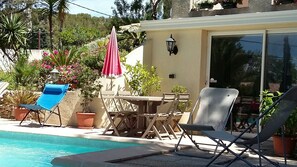 Uma área de piscina com espreguiçadeiras, uma mesa e plantas em vasos.