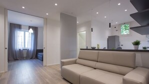 A modern living room with a sofa, a kitchen area with a counter and appliances, and a hallway leading to another room. -  Civico 88 Modern design (Padova)
