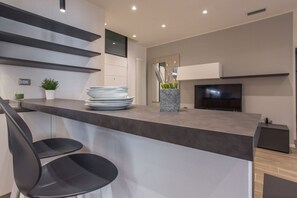 A modern kitchen with a bar area, a flat-screen TV, and a potted plant.