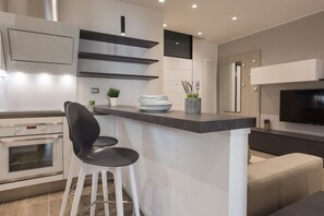 Une cuisine moderne dotée d’un four encastré, d’un coin bar avec des tabourets et d’un téléviseur à écran plat fixé au mur.