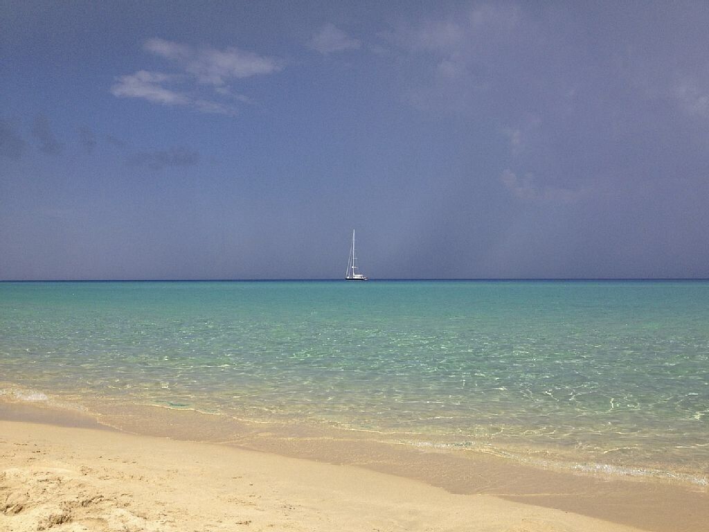 Uma praia com águas turquesa cristalinas e um veleiro ao longe.