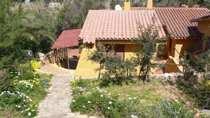 Um edifício amarelo com telhado de telhas vermelhas, rodeado por vegetação e um caminho de pedra.