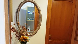 Un couloir avec un piédestal blanc, un miroir et une porte en bois.