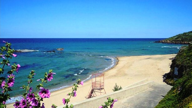 Une plage avec une eau d’un bleu limpide, un rivage sablonneux et un poste de surveillance pour les sauveteurs.