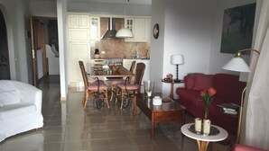 Una camera d'hotel con zona pranzo, soggiorno con divano, lampada e un quadro appeso al muro.