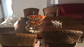Zona pranzo con sedie in vimini, un tavolo da pranzo con un centrotavola in vetro e un divano rosso sullo sfondo.