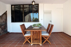Una mesa de madera con cuatro sillas, una planta en maceta y una ventana que ofrece vista a árboles y un edificio.