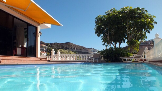 Una piscina con acqua cristallina e blu, circondata da un recinto bianco e un albero grande.