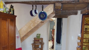 A rustic kitchen with wooden beams, a wooden chair, and a cabinet with various items on top. - The Lily Féliz, a pretty village house between Rodez and Albi (Centrès)