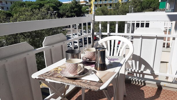 A balcony with a table set for two, featuring a coffee pot, cups, and saucers.