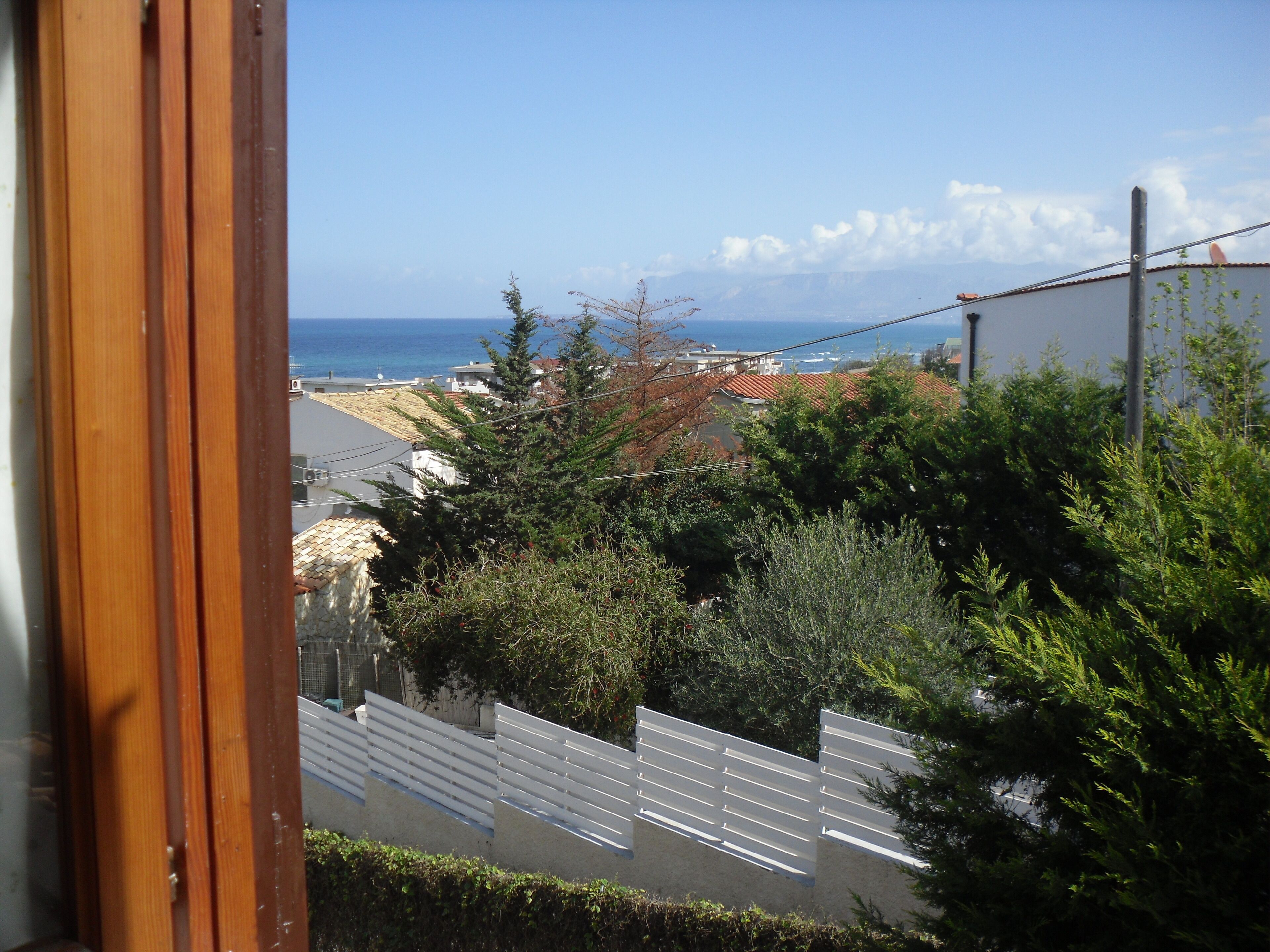 A coastal view with a wooden window frame, a white fence, and a building with a red roof.