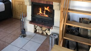 Une pièce chaleureuse avec une cheminée, des poutres apparentes, une tête de cerf accrochée au mur et une échelle menant à une mezzanine.