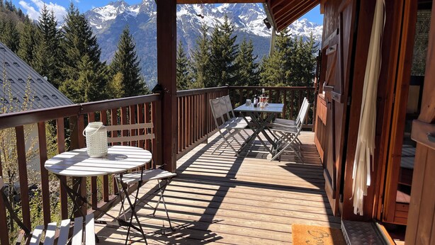Une terrasse en bois avec une table et des chaises, offrant une vue sur un paysage montagneux.