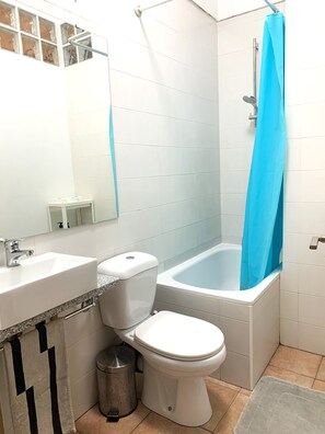 Ein Badezimmer mit Toilette, Waschbecken, Badewanne mit blauer Duschvorhang und Fliesenwand.