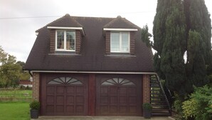 A two-story house with a dark roof and two garage doors. - A DELIGHTFUL STUDIO APARTMENT WITH FARM LAND VIEWS (Patching Nr.Arundel)