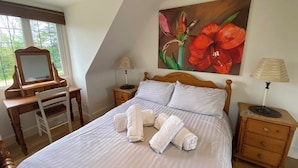A bedroom with a bed, a wooden desk, a chair, two bedside tables with lamps, and a large floral painting on the wall. - A DELIGHTFUL STUDIO APARTMENT WITH FARM LAND VIEWS (Patching Nr.Arundel)