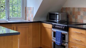 A kitchen with wooden cabinets, a black countertop, a microwave, a stove, and a window with a view of greenery. - A DELIGHTFUL STUDIO APARTMENT WITH FARM LAND VIEWS (Patching Nr.Arundel)