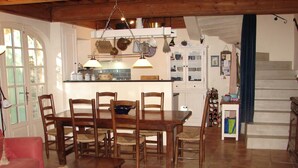 A cozy living room with a dining table, chairs, a coffee table, and a sofa. There is a kitchen area with cabinets and a wine rack.