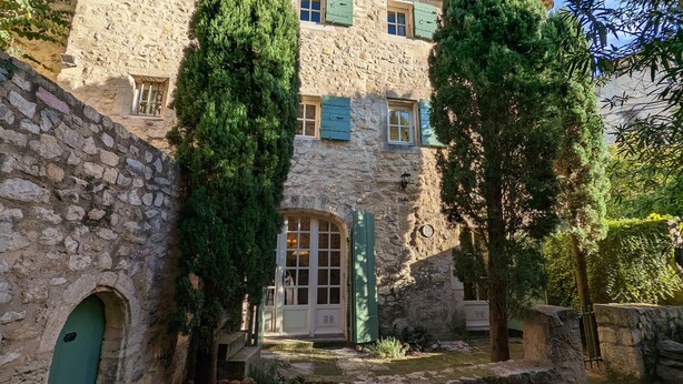 A stone building with a courtyard, a green door, and a window with shutters.